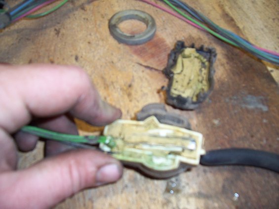Hand holding a disassembled electrical connector with green and black wires attached to a wooden surface