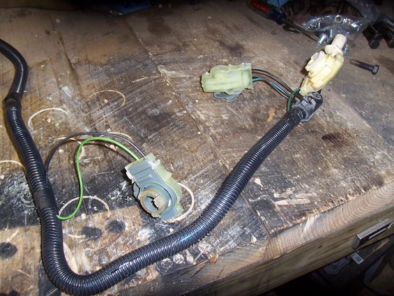 Wiring harness with black corrugated tubing and multiple electrical connectors, lying on a wooden surface