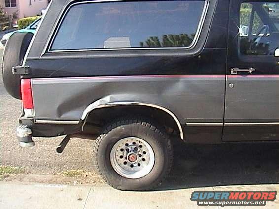 Rear passenger side of a black Ford Bronco with significant body damage to the quarter panel and a flat tire