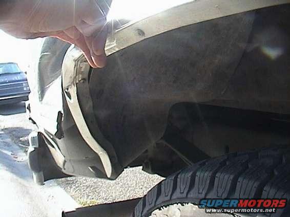 Close-up of a vehicle's rear wheel well and tire. A hand in a glove is touching the fender trim
