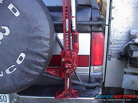 Red hi-lift jack on a 1987 Ford Bronco rear bumper, spare tire visible