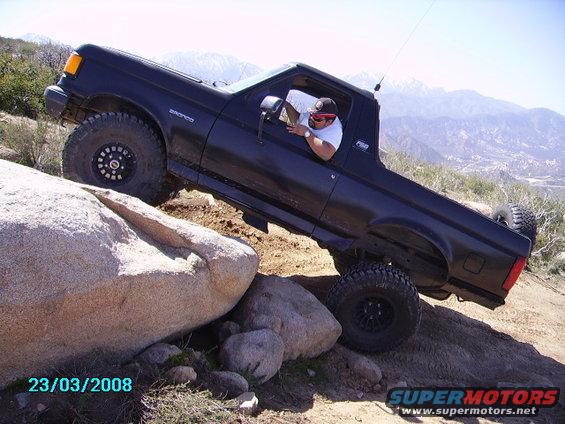 Black 1990 Ford Bronco climbing over large rocks on a trail