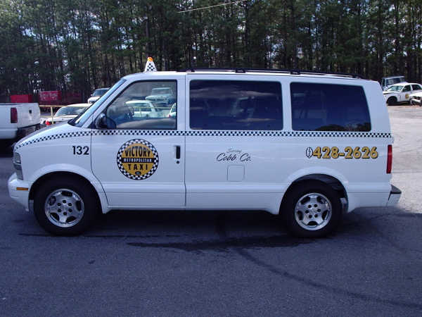 White taxi van with checkered stripe, number 132, and phone number 6428-2626