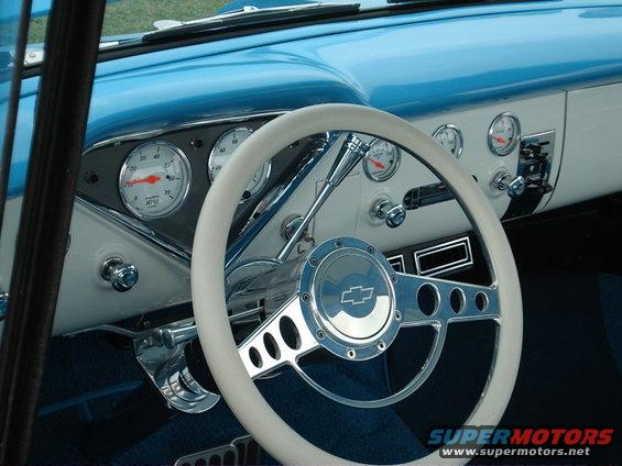 Interior view of a car with a white steering wheel, chrome horn button with Chevrolet logo, and multiple gauges on the dashboard