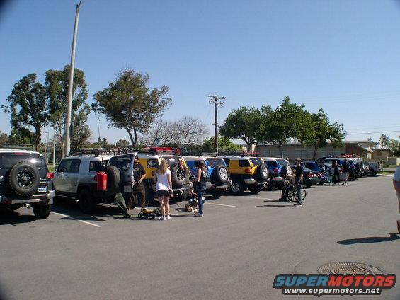 Several Toyota FJ Cruisers parked in a lot, some with people standing around them
