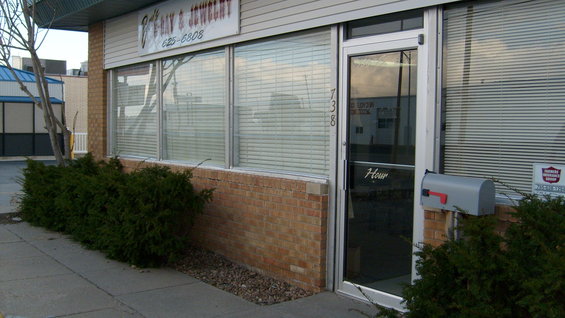 Storefront with brick base, large windows, and a glass door. A mailbox is mounted to the wall