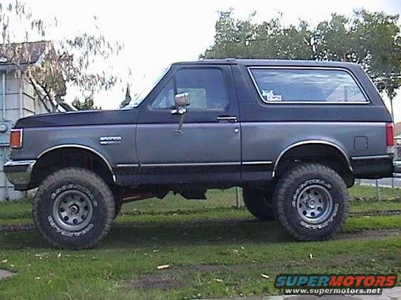 Two-tone gray 1990 Ford Bronco with lifted suspension and large tires, seen from the side