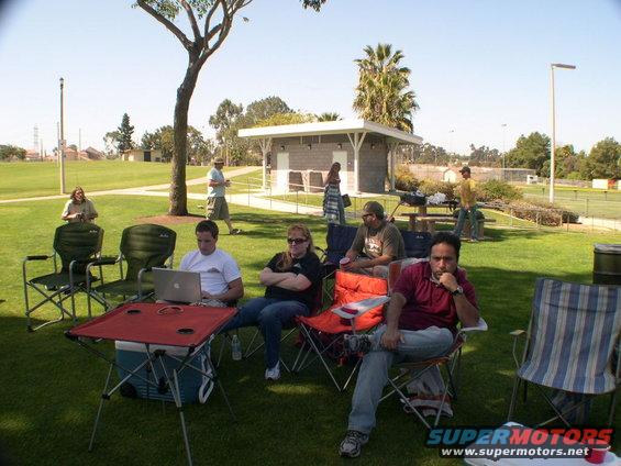 People sitting in chairs at a park, some with a laptop and cooler