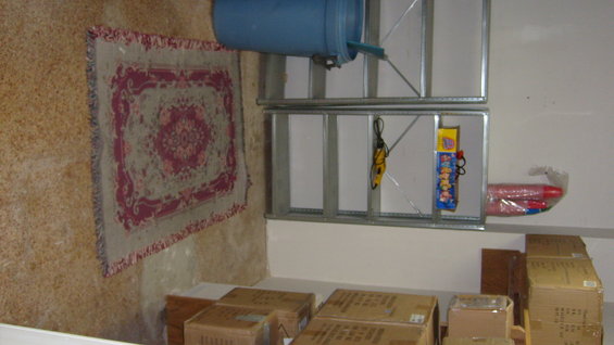 Interior storage area with shelves holding a blue barrel, rug, and boxes