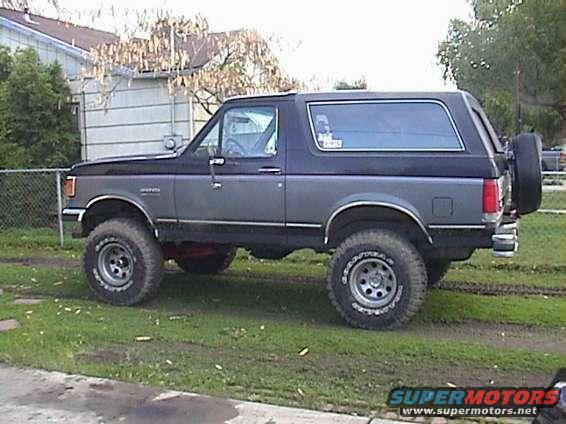 1990 Ford Bronco with lifted suspension and large tires, parked on grass