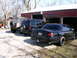 2001 Ford Crown Victoria - Three vehicles are parked outside a red garage. The sedan in the foreground is black with tinted windows.