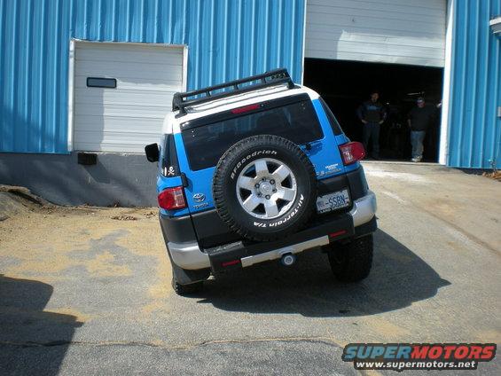 Blue and white Toyota FJ Cruiser with a spare tire on the rear, parked in front of a blue building