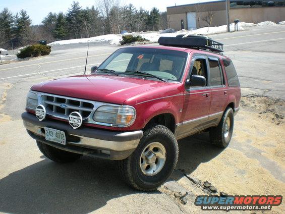 Red Ford Explorer with roof rack and off-road tires parked on a dirt patch