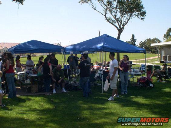 People gathered outdoors under blue tents on a grassy field
