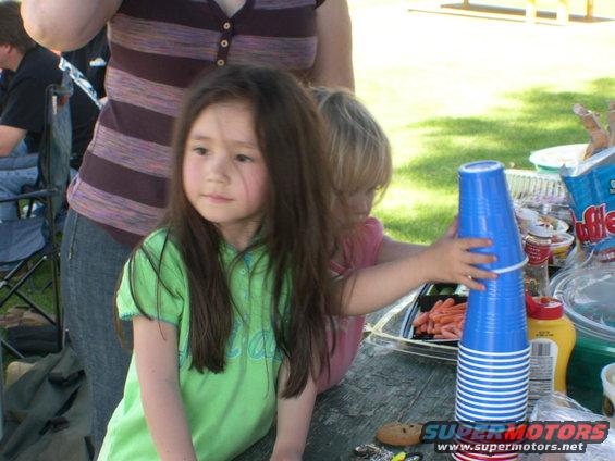 Two young children are at a picnic table with cups and food