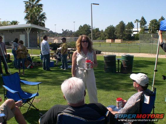 People gathered on a grassy field near a baseball diamond, some sitting in chairs