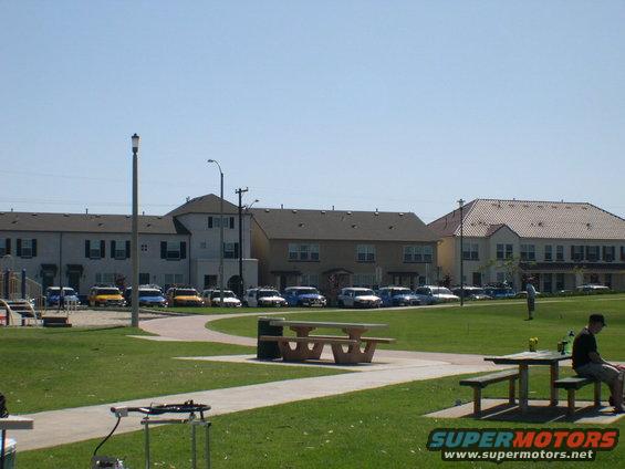 Parked cars in a lot with buildings and a park in the foreground
