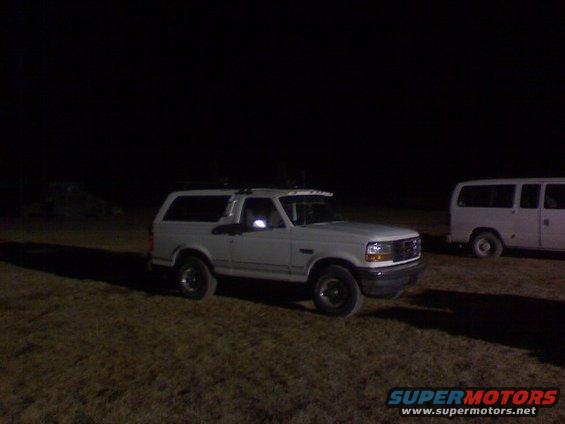 1995 Ford Bronco parked at night next to a white van