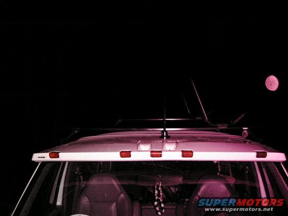 SUV roof with a light bar and antenna at night. Moon visible in the sky