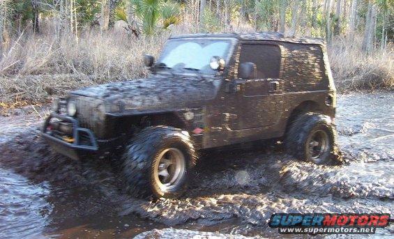 Mud-covered Jeep Wrangler driving through water and mud