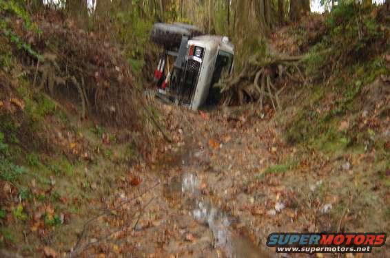 Off-road vehicle flipped onto its side in a wooded ditch with trees and roots around it