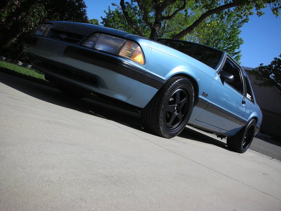 Blue 1990 Ford Mustang coupe with black five-spoke wheels parked on a driveway