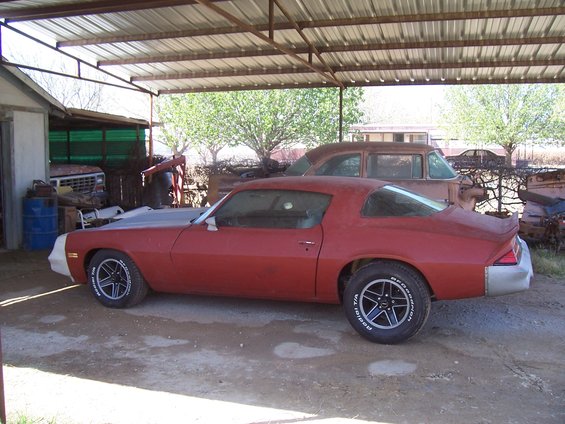 red coupe with gray hood, parked under a metal roof next to an old brown car