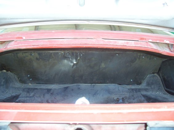 Trunk interior of a red car, showing the black lining and some dents in the metal panel