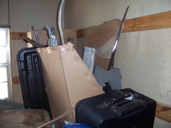 Pile of car parts and luggage in a cluttered room, with a chrome trim piece visible