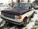 1988 Ford Bronco - A two-tone Ford Bronco sits in a snowy yard, showing its front end and driver's side.
