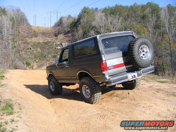 1989 Ford Bronco driving on a dirt trail with a spare tire mounted on the rear
