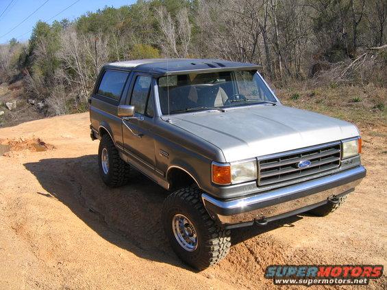1989 Ford Bronco parked on dirt with trees in background