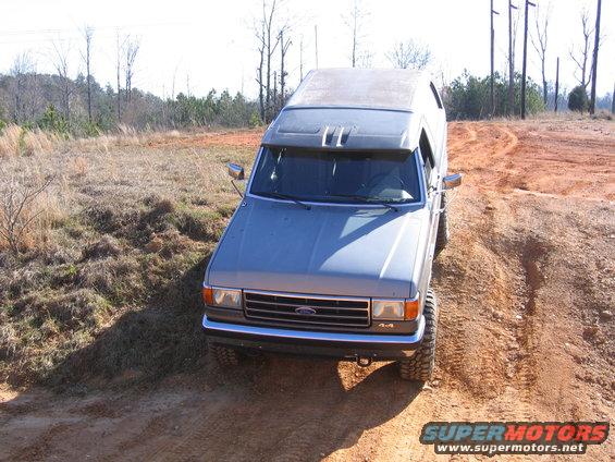 Gray Ford Bronco driving on dirt road. Has a roof rack and off-road tires