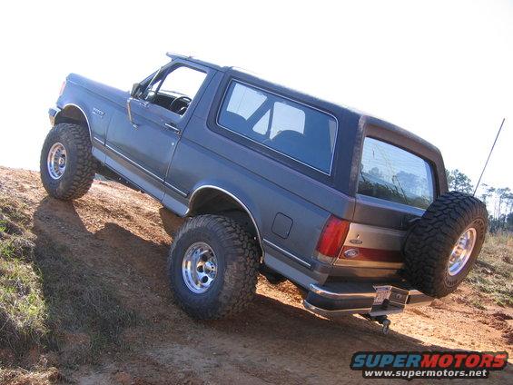 Gray 1989 Ford Bronco climbing a dirt hill, rear-mounted spare tire visible
