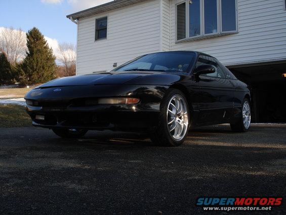 Black 1993 Ford Probe with aftermarket wheels parked in front of a house