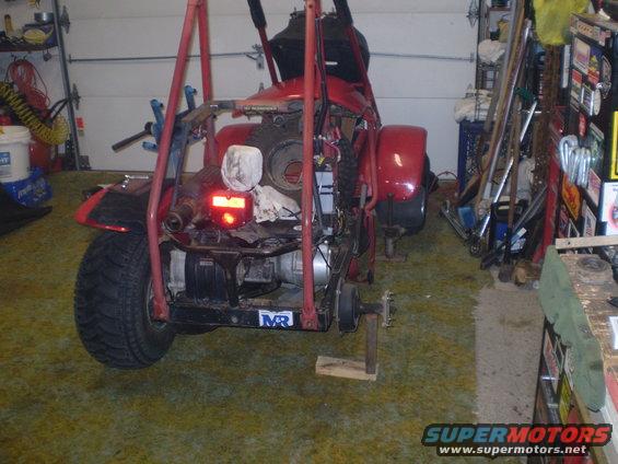 Red ATV chassis suspended by a red hoist in a garage. Visible is the engine, rear axle, and one tire
