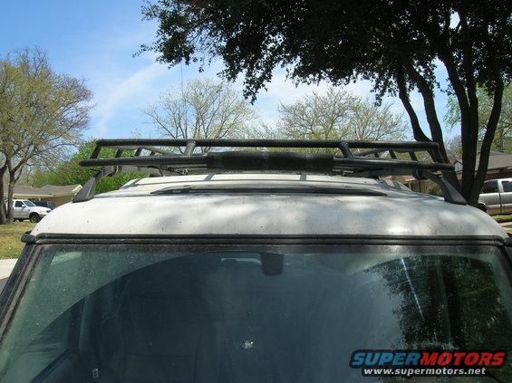 Top view of a white SUV with a black roof rack, parked outside. Another truck is visible in the background