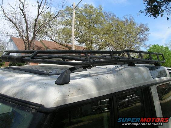 White SUV roof with a black metal roof rack, side view. Sunroof visible