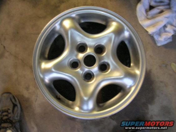 Silver five-spoke alloy wheel on a concrete floor, with a shoe and cloth in the background