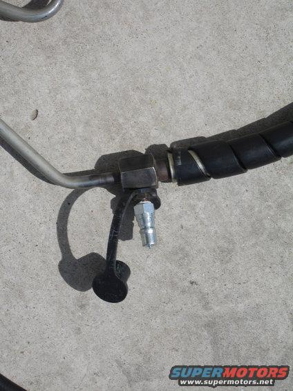 Close-up of a metal power steering hose with a black protective wrap and a quick-connect fitting