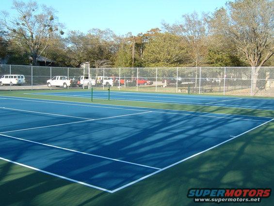 Tennis court with several white vans and trucks parked behind a fence