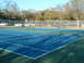 1979 Ford Ranchero - A bright blue tennis court is in the foreground, with a line of vehicles parked beyond the net and fence.
