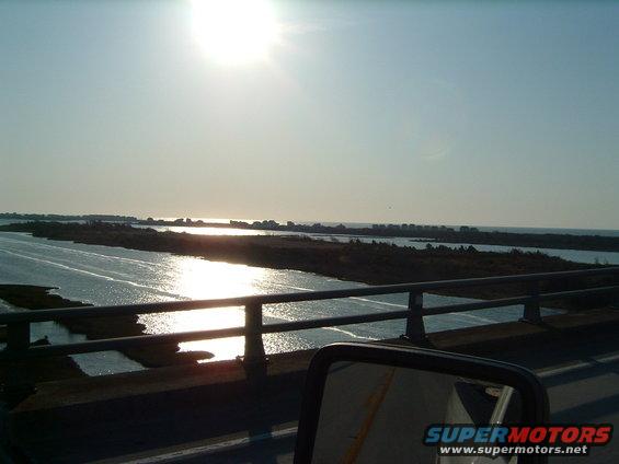 Side mirror view of a waterway with sun glare and distant shore