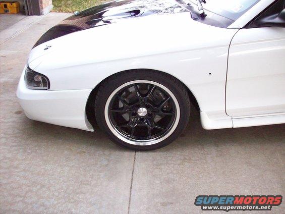 Front fender and wheel of a white 1997 Ford Mustang with black racing stripes on the hood