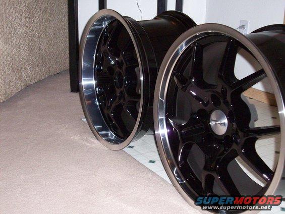 Two black aftermarket wheels with polished lips and five split spokes
