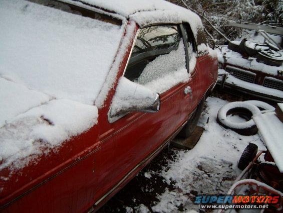 red car covered in snow, another car and tires in background