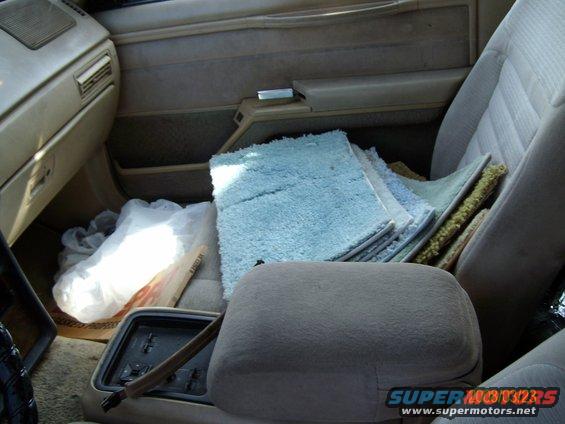 Car interior showing stacked rugs and a plastic bag on the floor