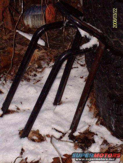 Black metal frame parts resting in snow next to a tire