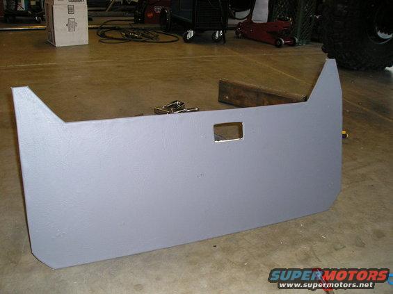 Gray door panel with a square cutout, lying on a concrete floor