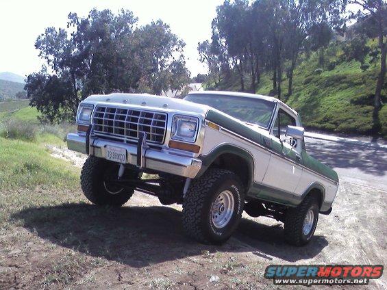 1978 Ford Bronco with white and green paint, lifted suspension, and off-road tires parked on a dirt incline